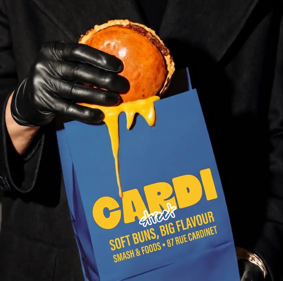 Sac Cardi Street bleu, tenu avec un gant noir, cheddar fondu qui coule sur le burger